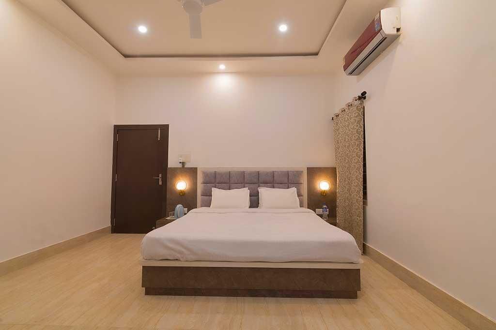 A modern hotel room with a large bed, a ceiling fan, an air conditioning unit, and a door.