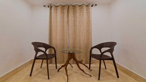 A room with a round glass table and two wicker chairs. - Royal Vista (Jorhat)