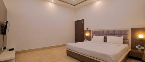 A modern bedroom with a bed, a ceiling fan, recessed lighting, and a nightstand with a lamp.