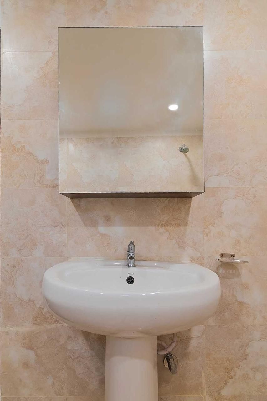 A bathroom with a white sink, a mirror above it, and beige tiled walls.