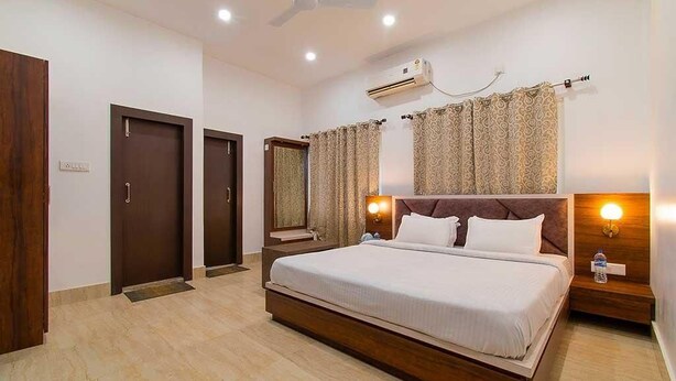 A hotel room with a large bed, a ceiling fan, an air conditioning unit, and a window with curtains. - Royal Vista (Jorhat)