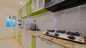 A modern kitchen with white cabinets, a granite countertop, a gas stove, and a microwave. - Royal Vista (Jorhat)