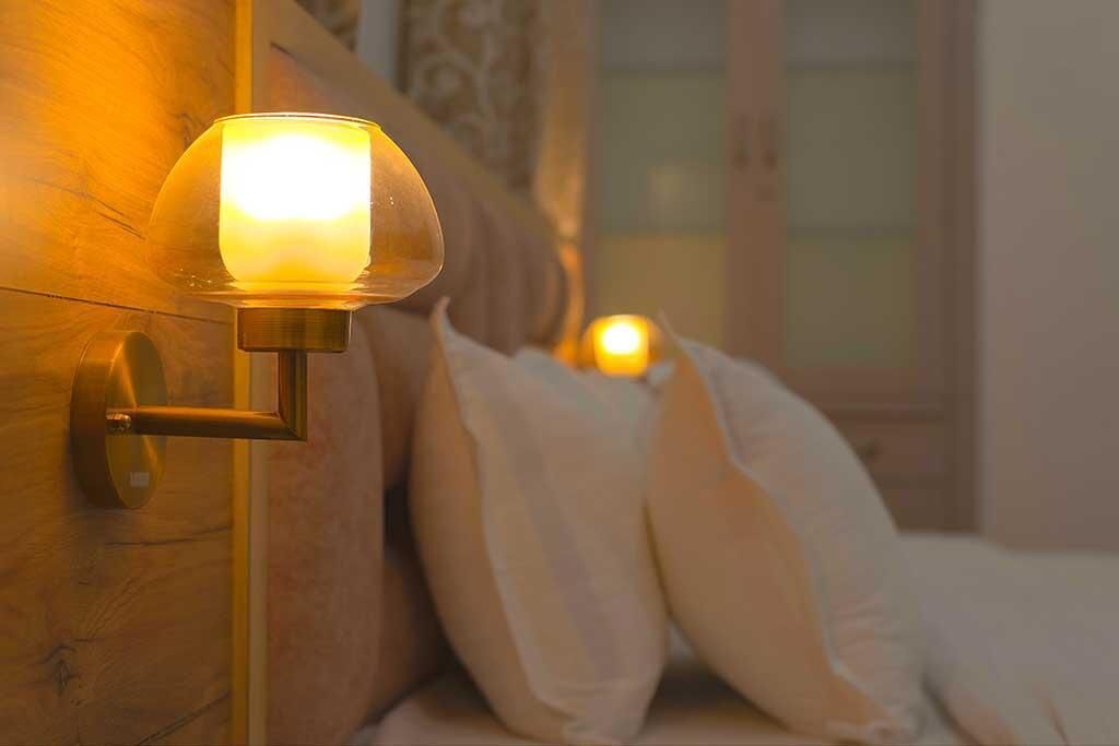 Een bedlamp met een glazen kap, een nachtkastje van hout en een bed met wit beddengoed.