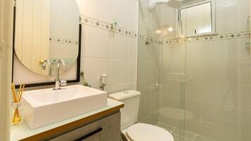 A bathroom with a white sink, a mirror, a toilet, and a glass-enclosed shower.