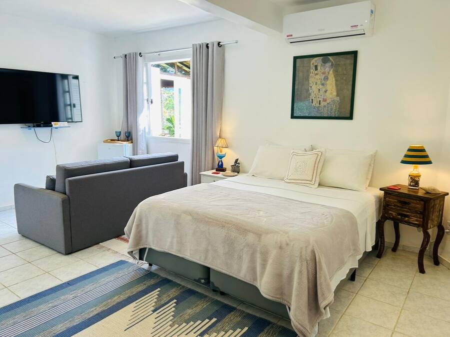 A bedroom with a bed, a sofa, a TV, a painting, and a lamp.