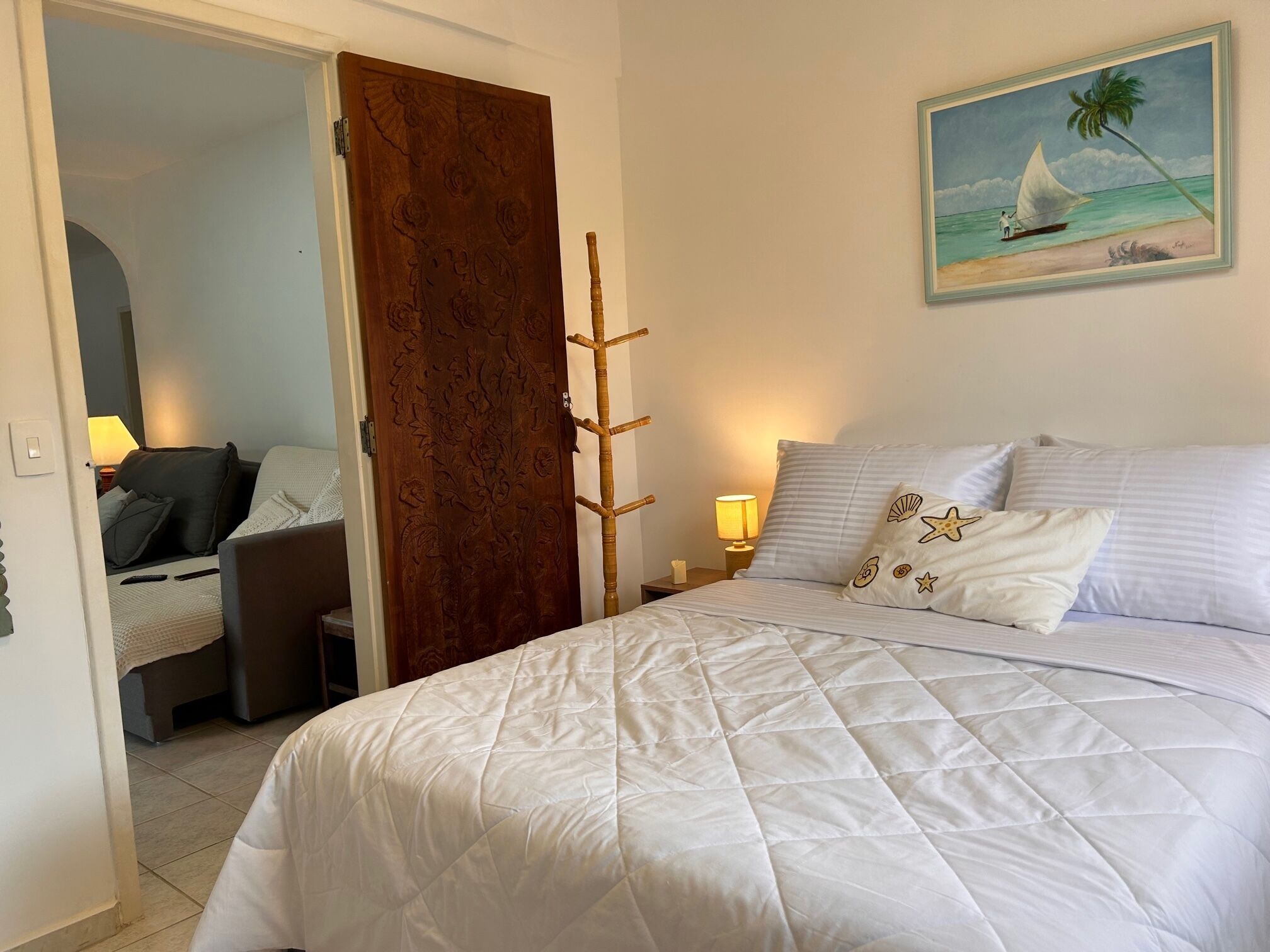 A hotel room with a bed, a desk, a chair, a wooden door, and a painting of a sailboat on the wall.