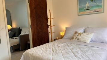 A hotel room with a bed, a desk, a chair, a wooden door, and a painting of a sailboat on the wall.