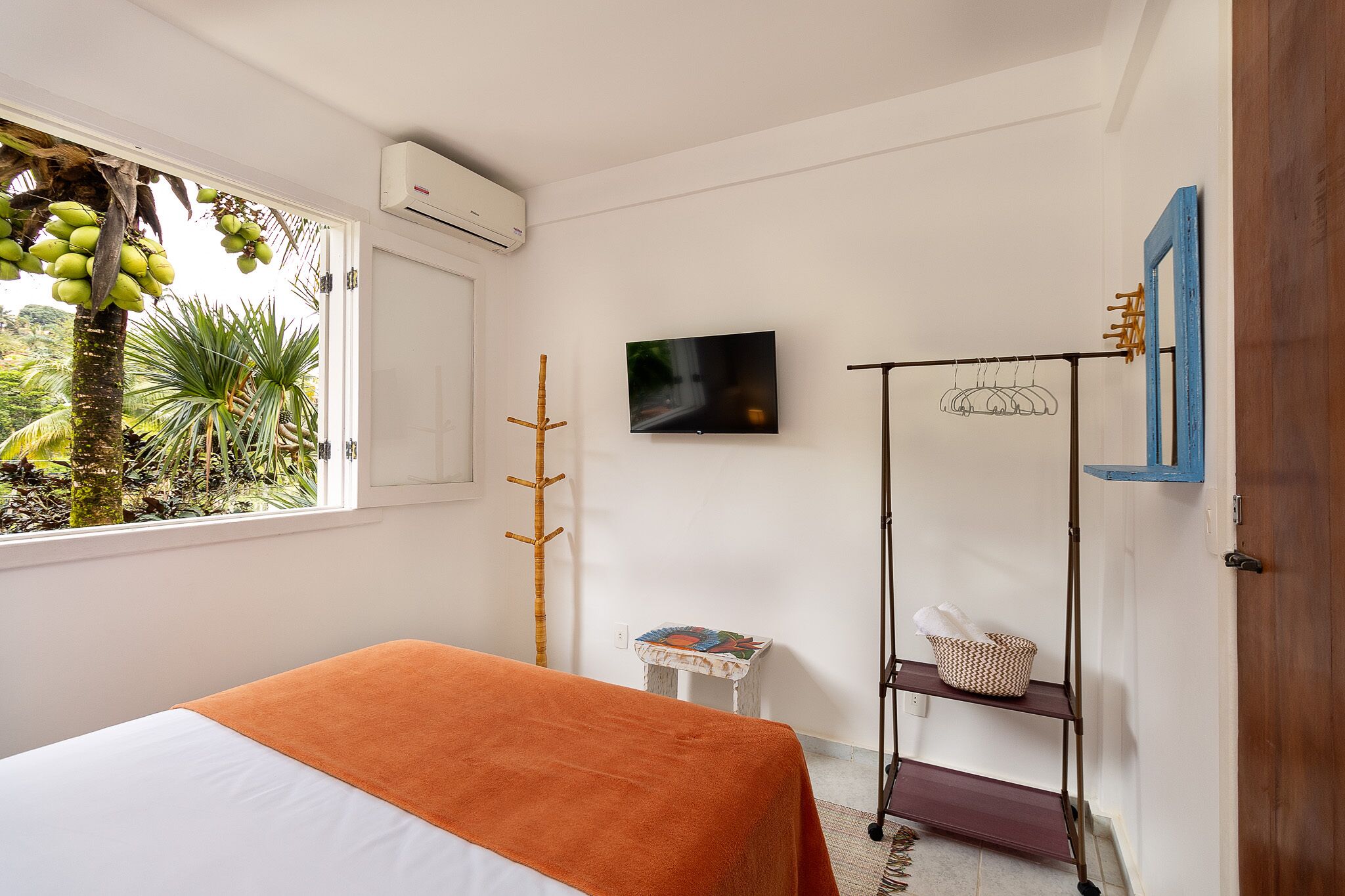 Una camera da letto con un letto, una televisione, un armadio, una finestra vista sul verde e un tavolino con un cesto.