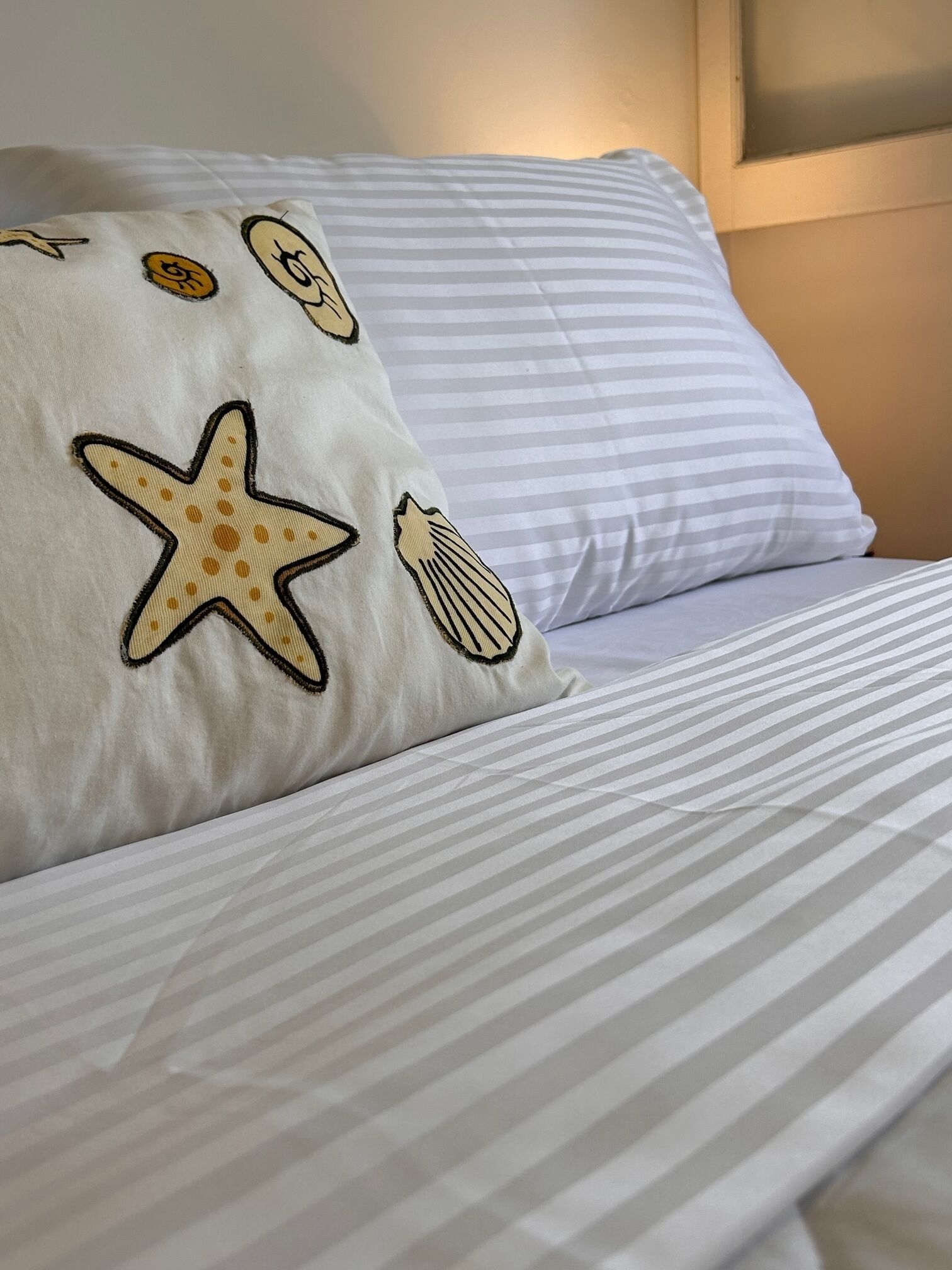Un lit avec une literie à rayures et un oreiller orné d’étoiles de mer et de coquillages brodés.