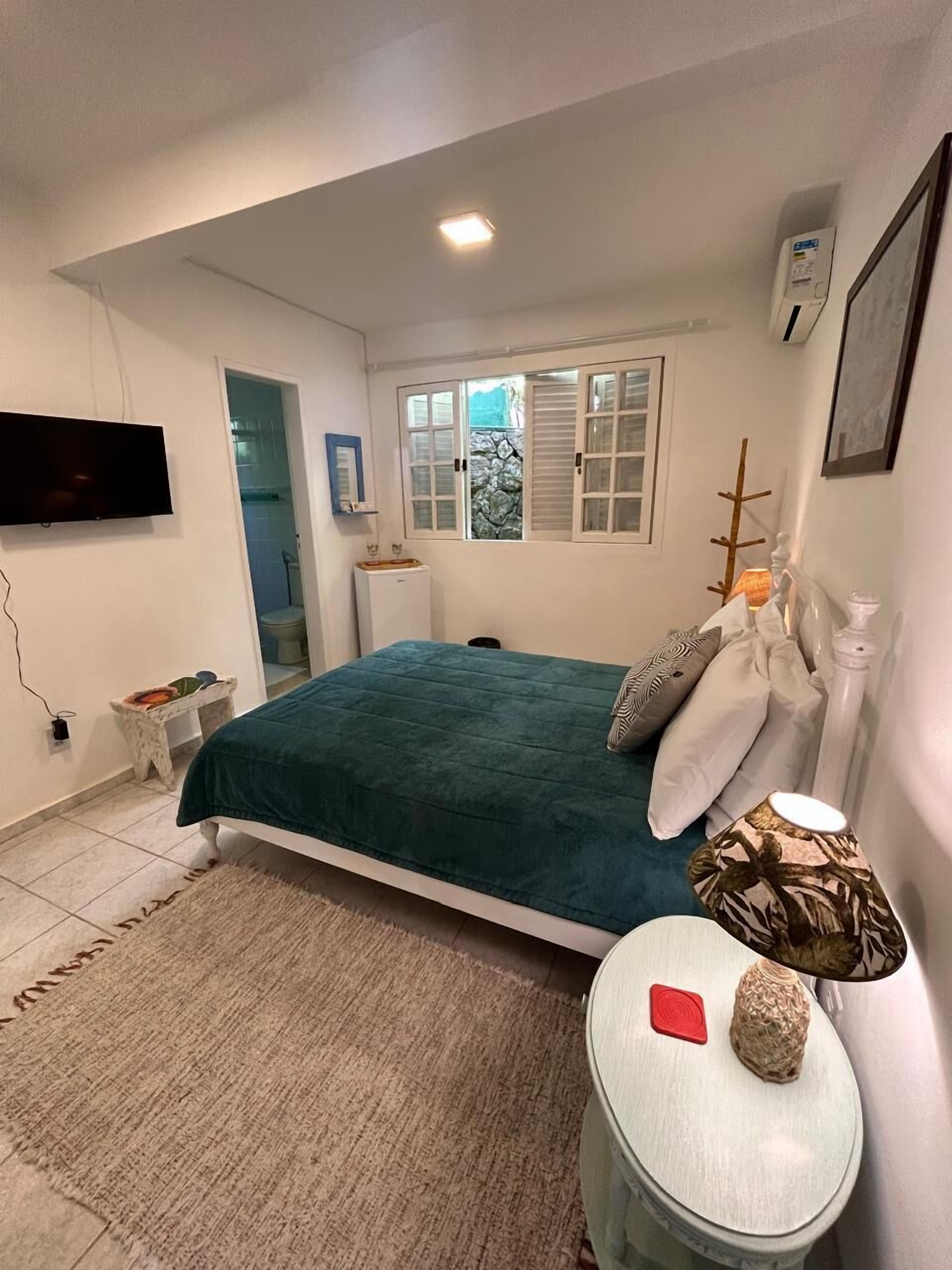 Un dormitorio con cama, mesita de noche, lámpara y televisor fijado a la pared.