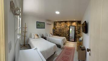 A hotel room with two beds, a stone wall, a TV, and a wooden coat rack.