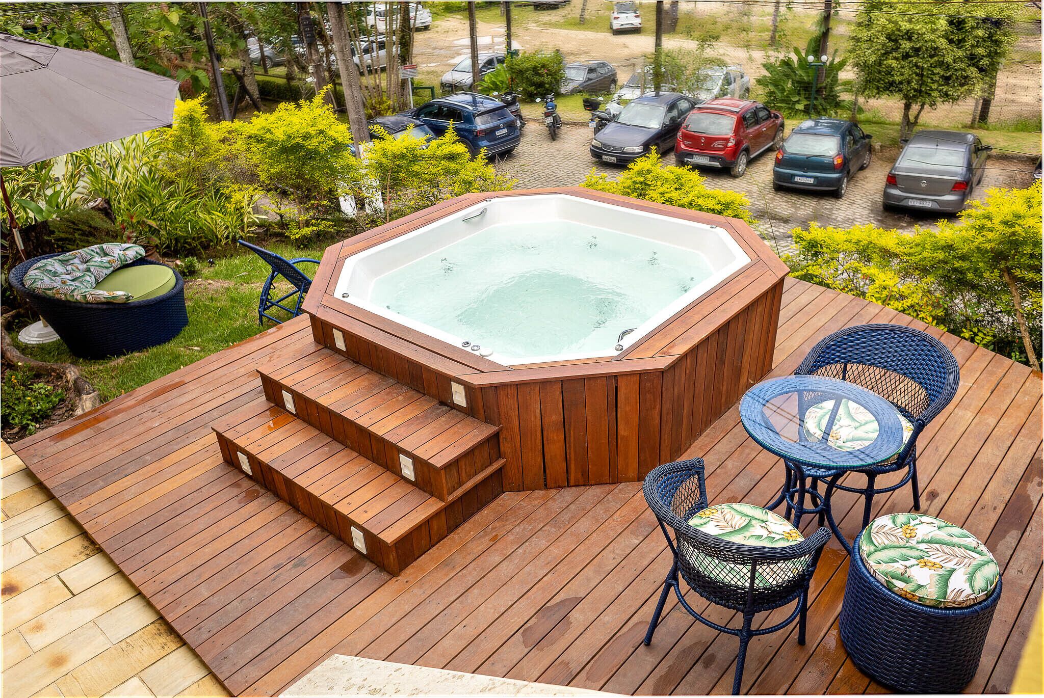 A hot tub on a wooden deck with steps leading up to it, surrounded by outdoor furniture.