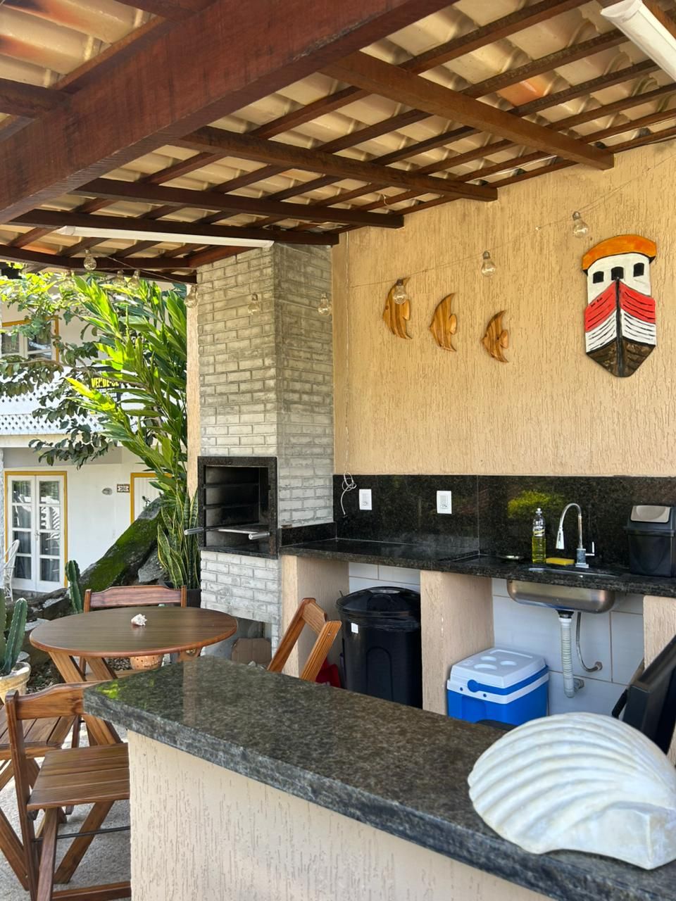 An outdoor kitchen with a brick wall, a sink, and a grill. There are wooden chairs and a table.
