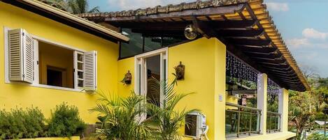 A yellow building with white shutters, a glass door, and a small balcony with potted plants.