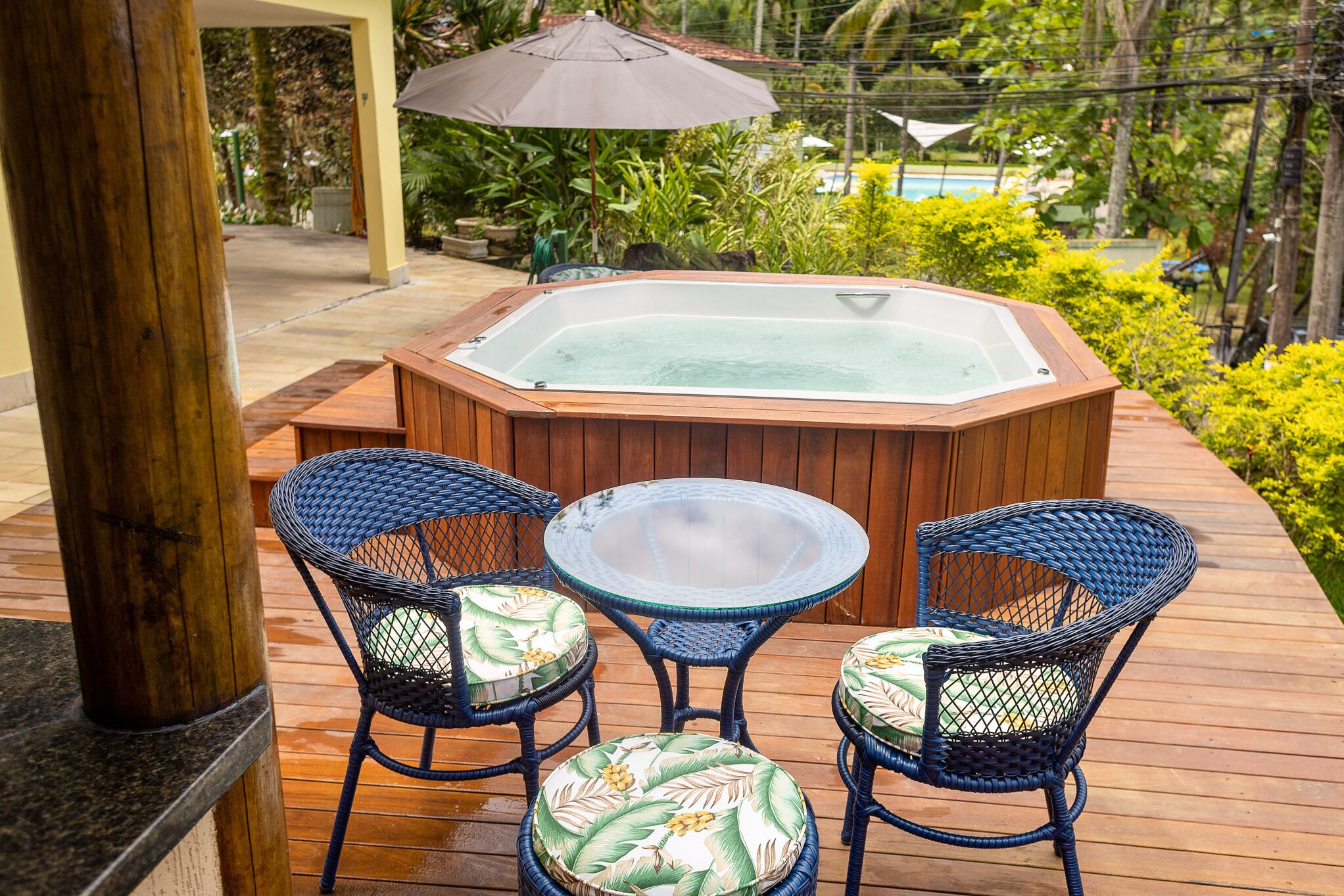 A wooden deck with a hot tub, two wicker chairs with cushions, and a glass table.