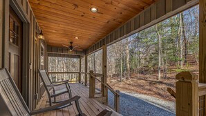 A covered porch with wooden flooring, two rocking chairs, and a view of a forested area. - 5-Star Cabin w/Hot Tub, Game Room, & Resort Perks! (Ellijay)