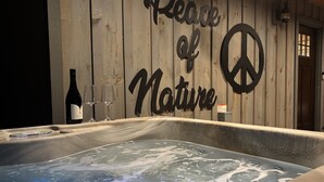 A hot tub with a wooden wall behind it, featuring a 'Peace of Nature' sign and a bottle of wine. - 5-Star Cabin w/Hot Tub, Game Room, & Resort Perks! (Ellijay)