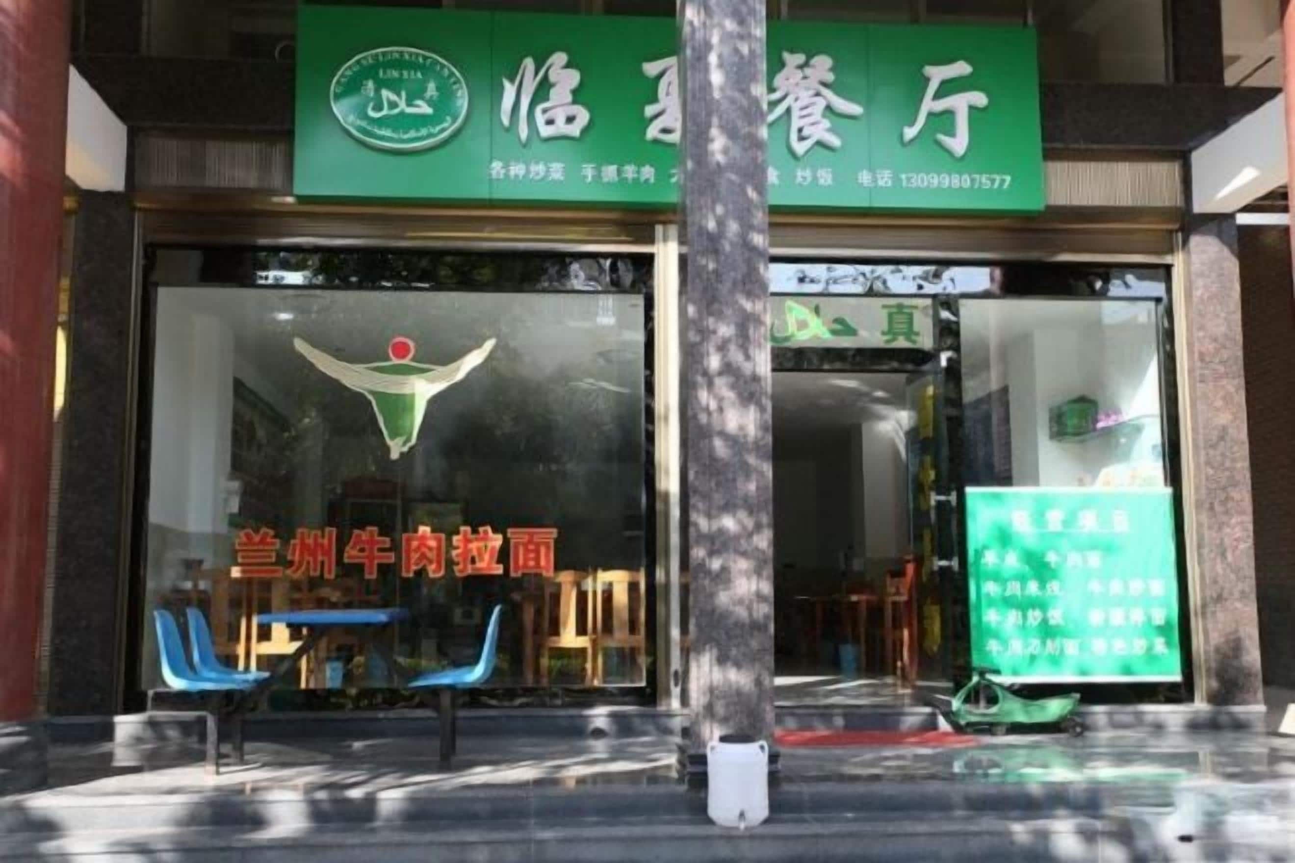 Un restaurant avec une enseigne verte, une fenêtre en verre et quelques chaises à l’extérieur.