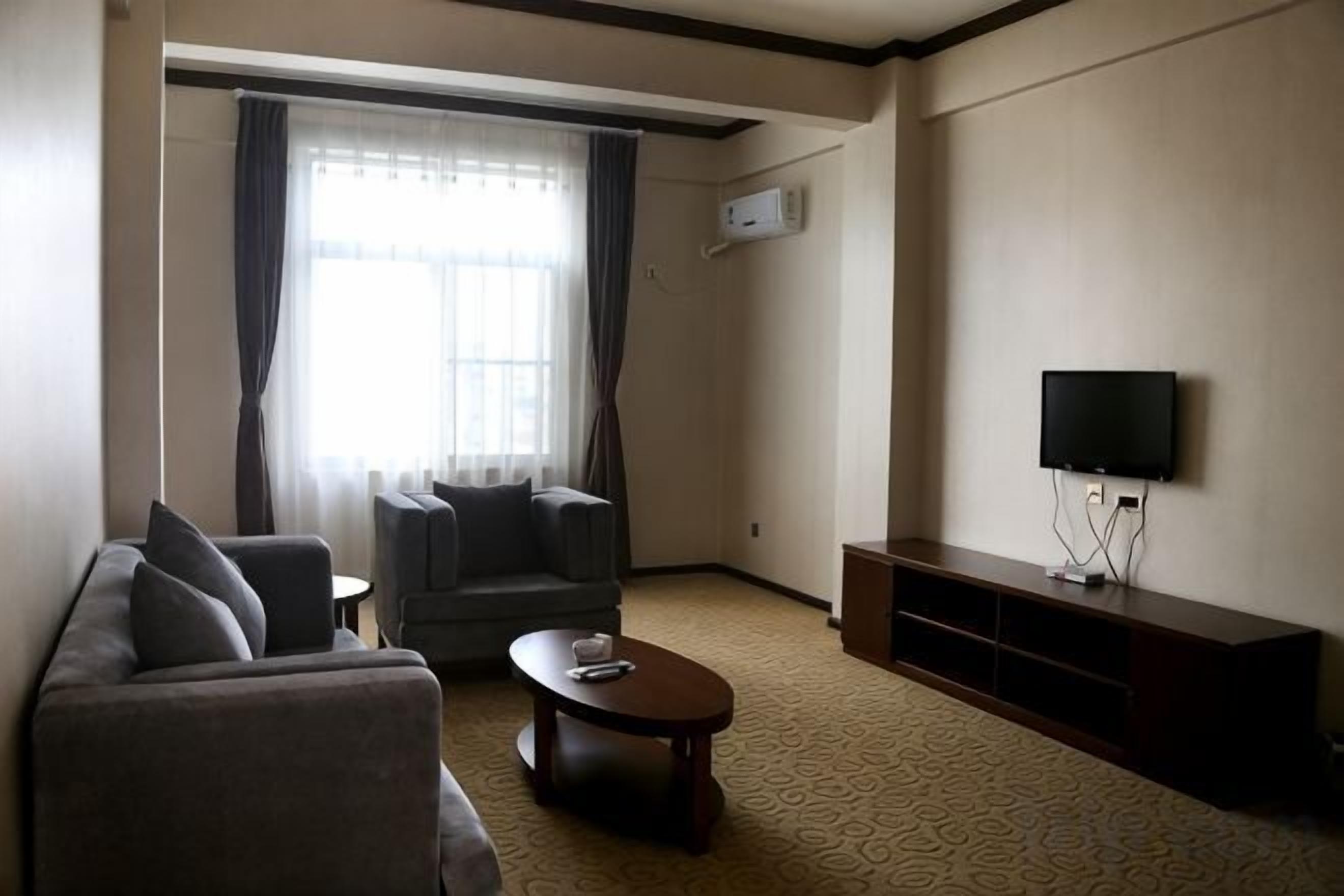 A living room with a sofa, armchair, coffee table, flat-screen TV, and a window with curtains.