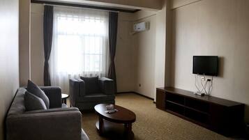 A living room with a sofa, armchair, coffee table, flat-screen TV, and a window with curtains.