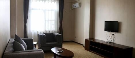 Una sala de estar con sofá, sillón, mesa de centro, televisor de pantalla plana y un ventanal con cortinas.
