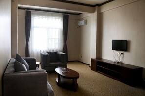 A living room with a sofa, armchair, coffee table, flat-screen TV, and a window with curtains. - Heping Hotel (Gejiu)