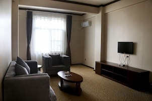 Una sala de estar con sofá, sillón, mesa de centro, televisor de pantalla plana y un ventanal con cortinas.
