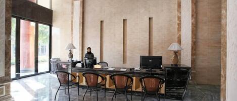 A modern hotel lobby with a marble floor, a reception desk, and a large chandelier.