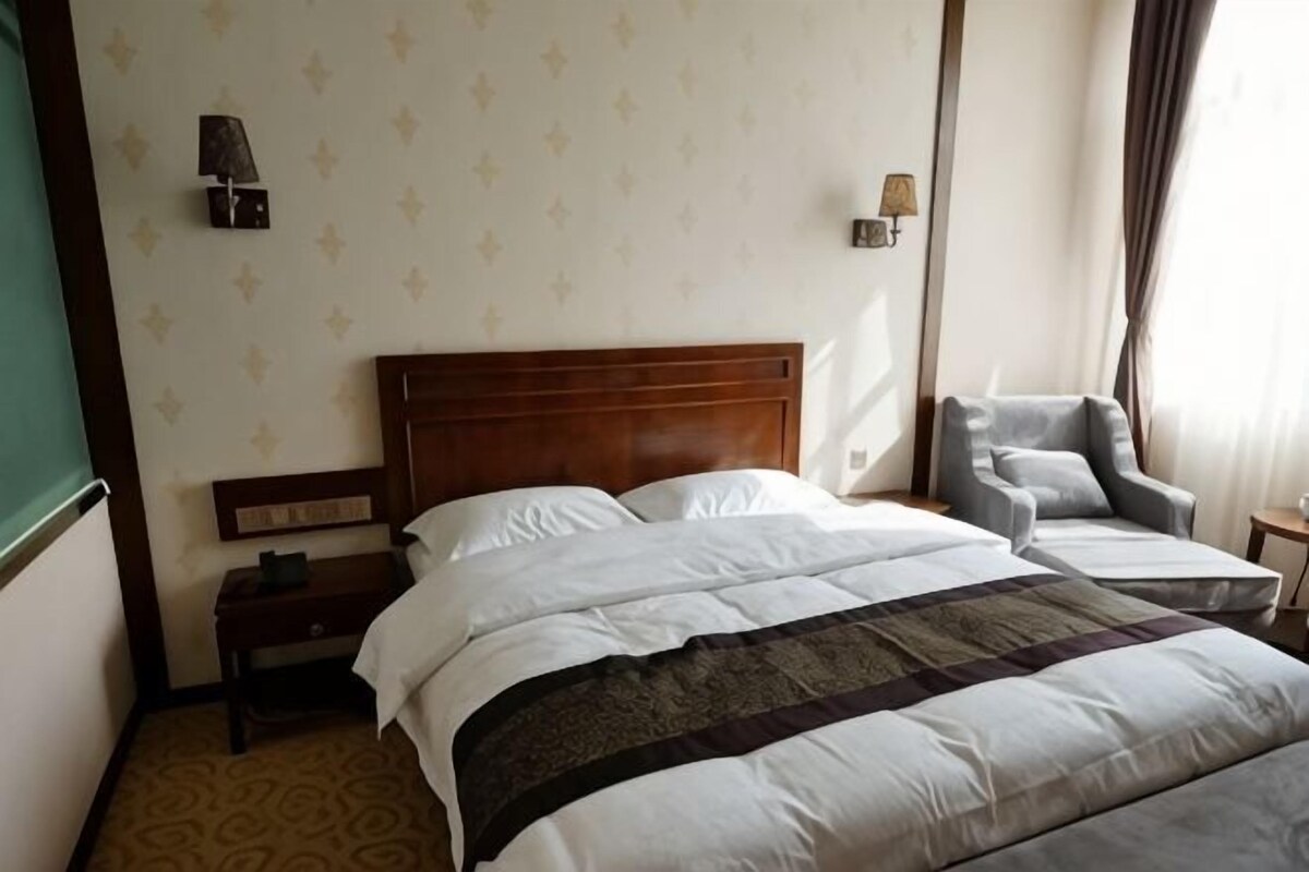Een hotelkamer met een tweepersoonsbed, een nachtkastje, een stoel en een wandlamp.