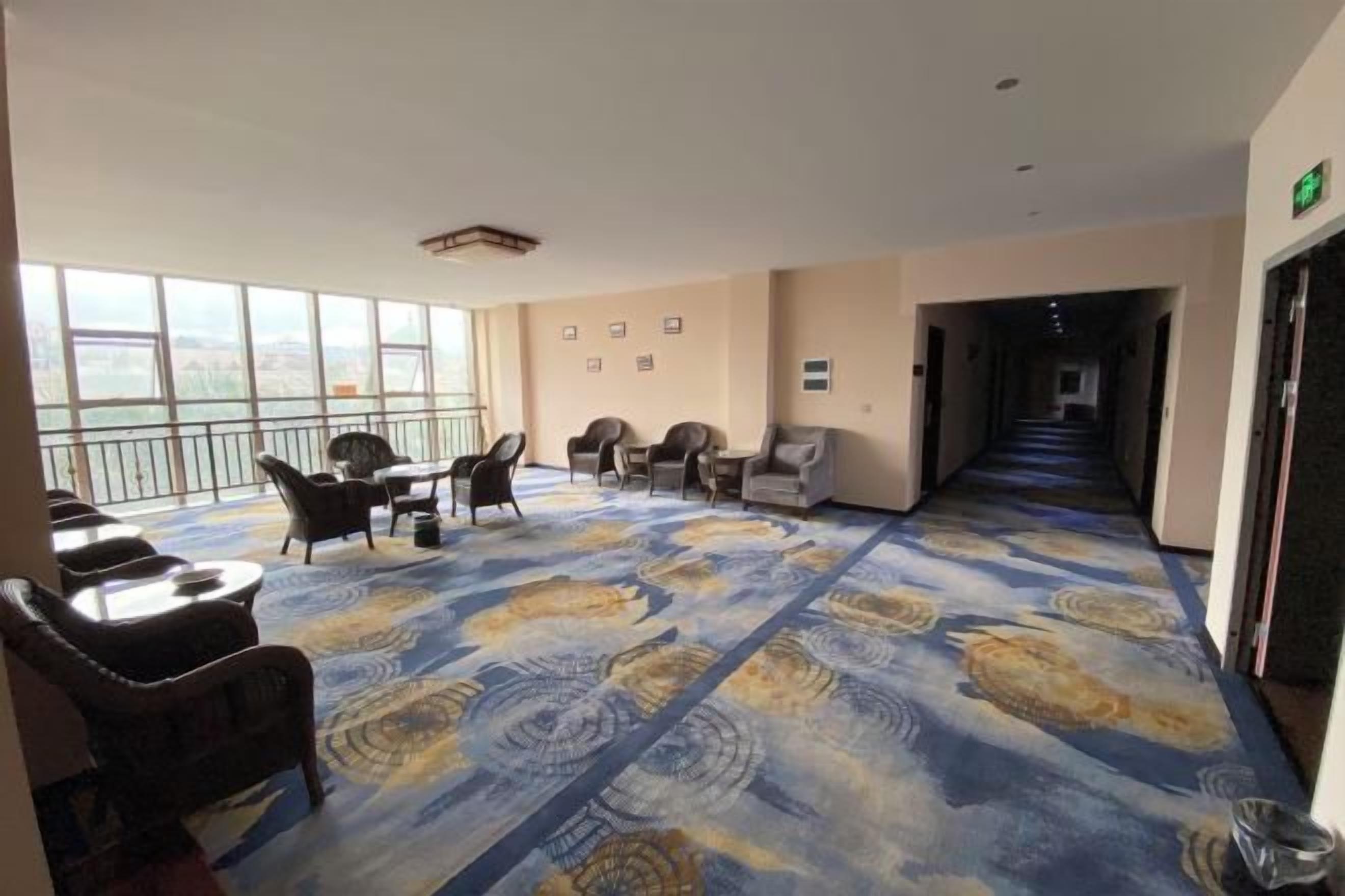 A hotel room with a large window, a patterned carpet, and a seating area with chairs and a table.