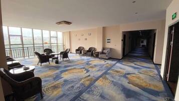 A hotel room with a large window, a patterned carpet, and a seating area with chairs and a table.