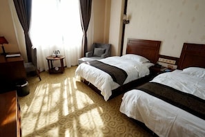 A hotel room with two beds, a chair, a small table, and a lamp.