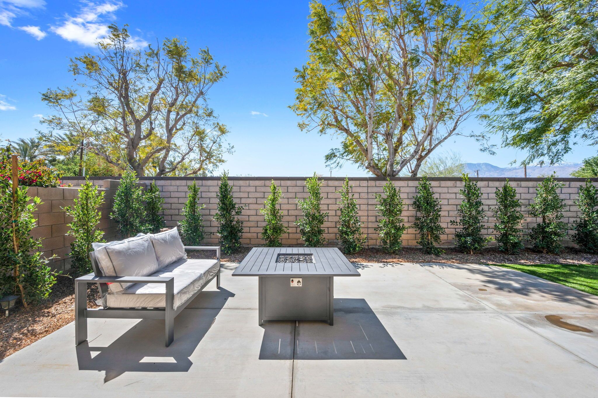 An outdoor patio with a metal table and a sofa, surrounded by a brick wall and small plants.