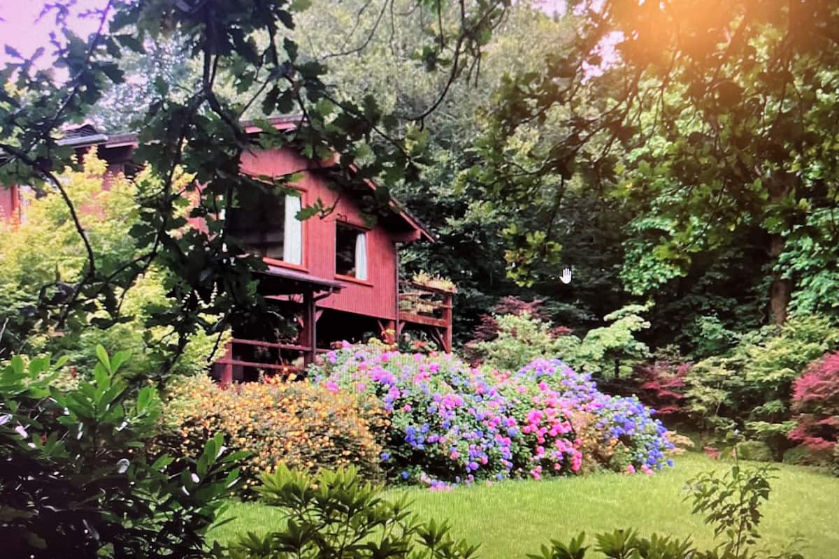 A red house surrounded by lush greenery and colorful flowers.