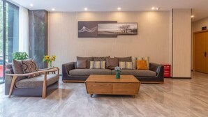 A modern living room with a sofa, armchair, and coffee table, featuring artwork on the wall and a vase with flowers. - Kaise Hotel (Lijiang Bailong Square Branch) (Lijiang)