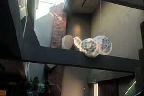 Un interior moderno con un diseño geométrico en el techo, un objeto esférico colgante y una planta.