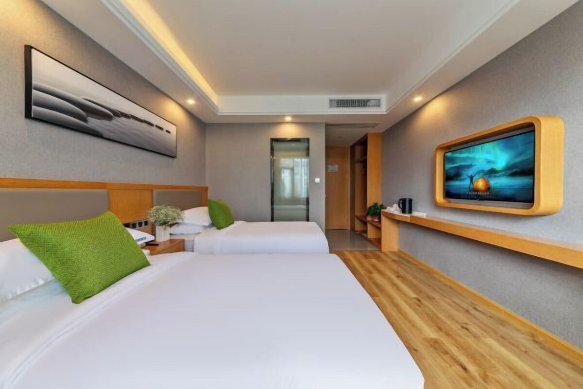 A modern hotel room with two beds, a TV, and a wooden accent wall.