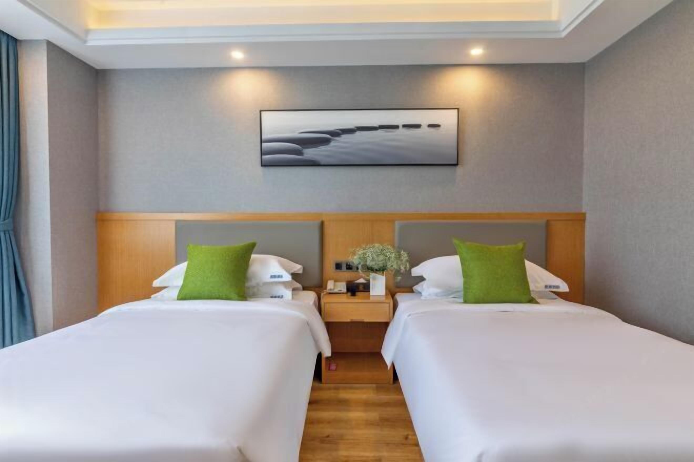 A hotel room with two beds, a wooden headboard, a nightstand with a vase of flowers, and a painting on the wall.