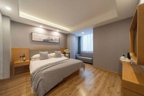 A modern hotel room with a large bed, a wooden nightstand, a bedside table, a sofa, and a large mirror. - Kaise Hotel (Lijiang Bailong Square Branch) (Lijiang)