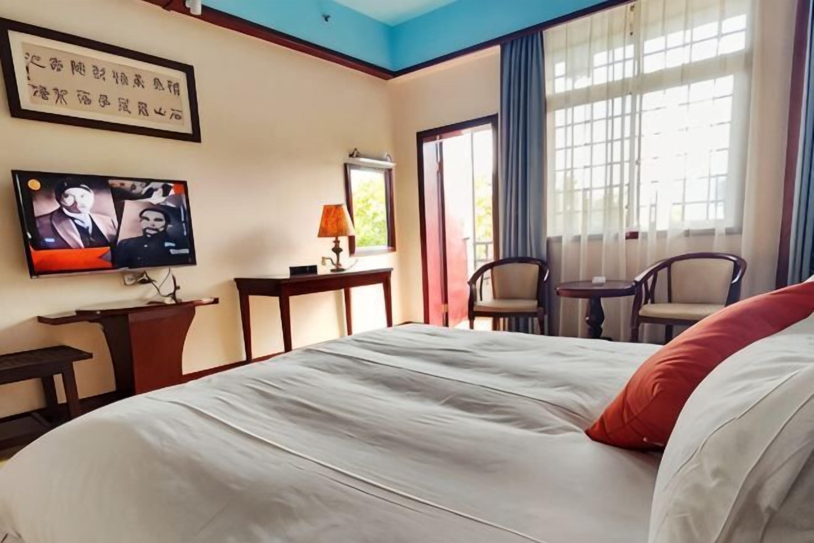 A hotel room with a bed, television, desk, lamp, chairs, and a window with curtains.
