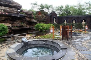 A traditional garden with a stone hot spring, rock formations, and statues.