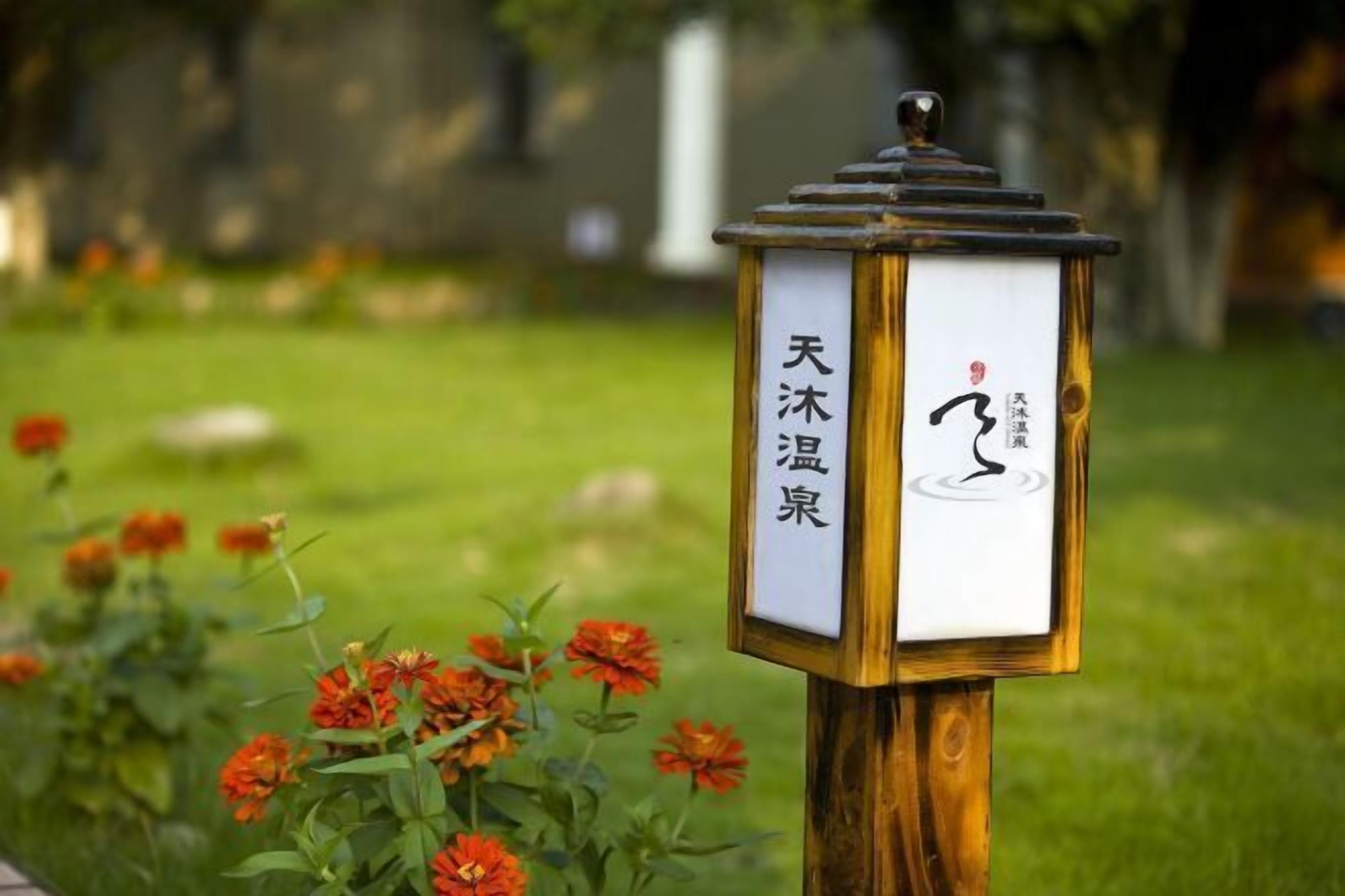 Un llum tradicional japonesa amb caràcters xinesos, situada en un jardí ple de flors taronja.
