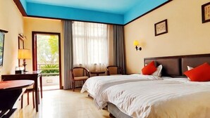 Quarto de hotel com duas camas, uma escrivaninha, cadeiras, um abajur e vista para o verde.