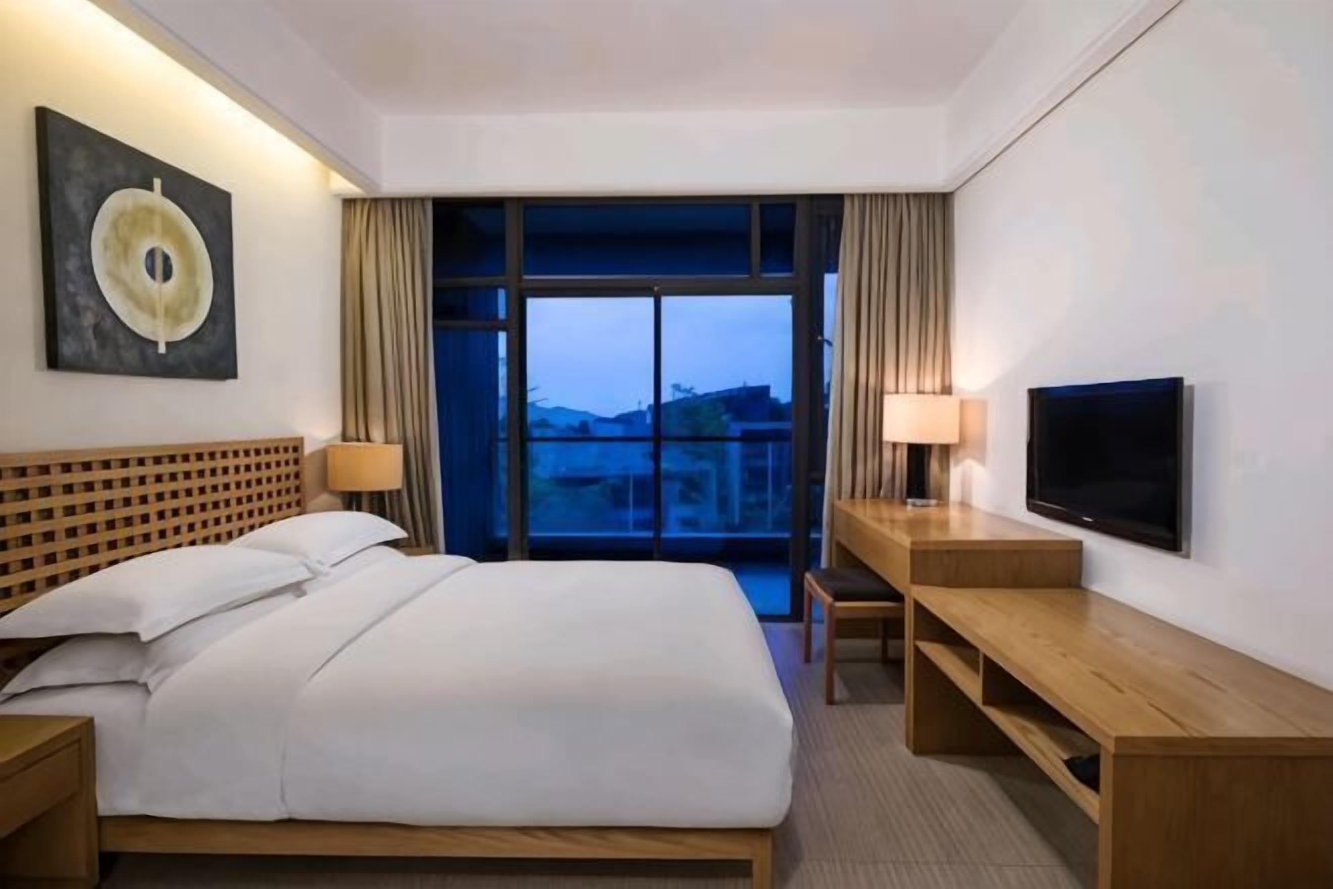 Een hotelkamer met een bed, een televisie, een bureau en een groot raam met gordijnen.