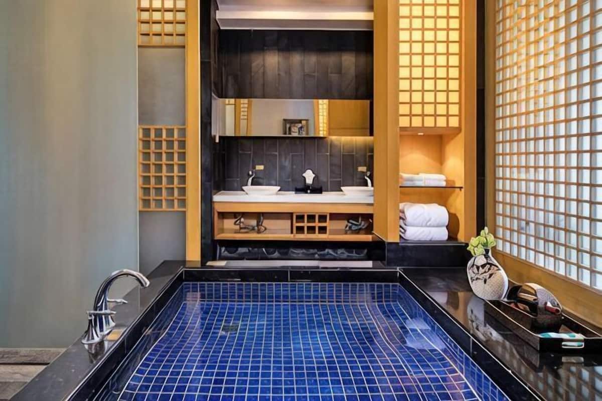 A modern bathroom with a blue-tiled hot tub, a sink with a mirror, and a shelf with towels.
