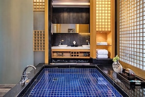 A modern bathroom with a blue-tiled hot tub, a sink with a mirror, and a shelf with towels.