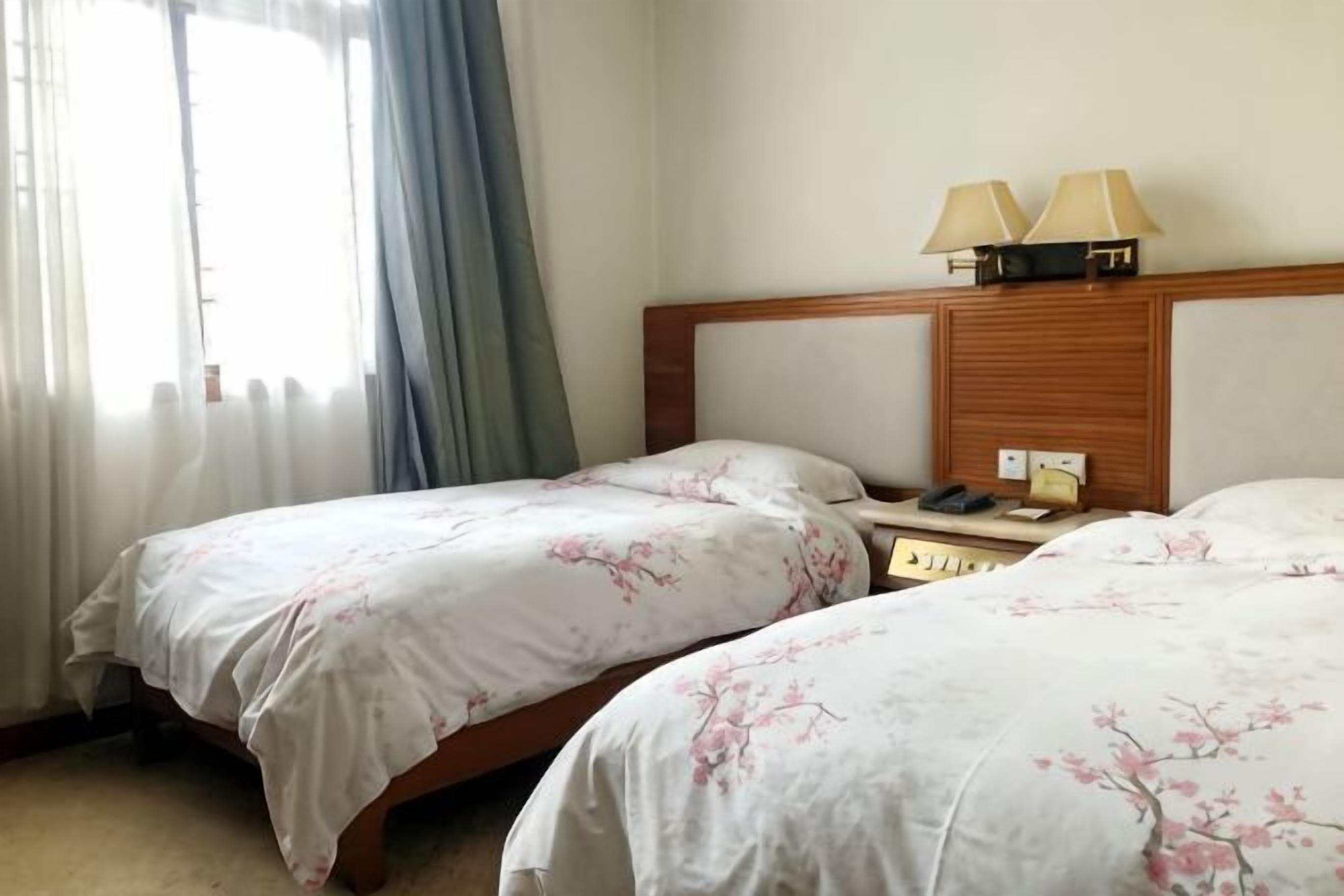 A hotel room with two beds, a wooden headboard, two bedside lamps, and a window with curtains.