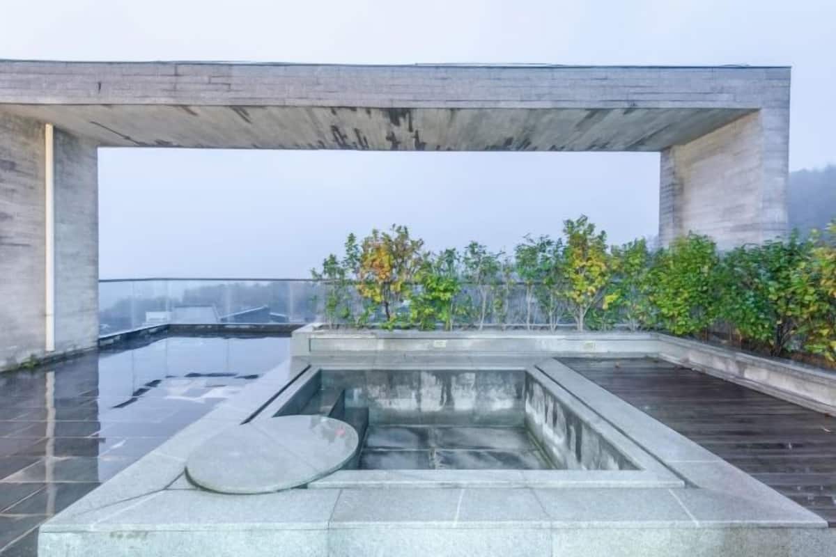 A rooftop pool with a concrete structure, surrounded by greenery.