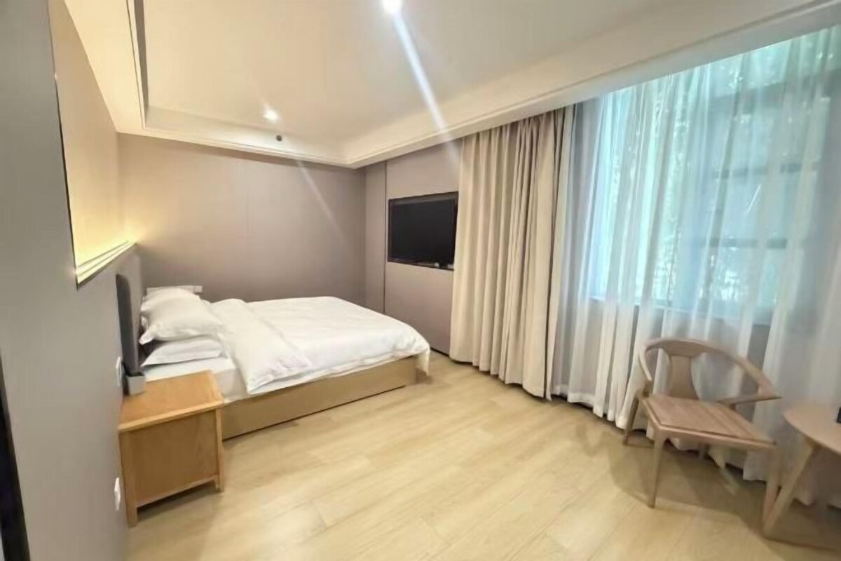 Habitación de hotel con cama, escritorio, silla, televisor y una ventana grande con cortinas.