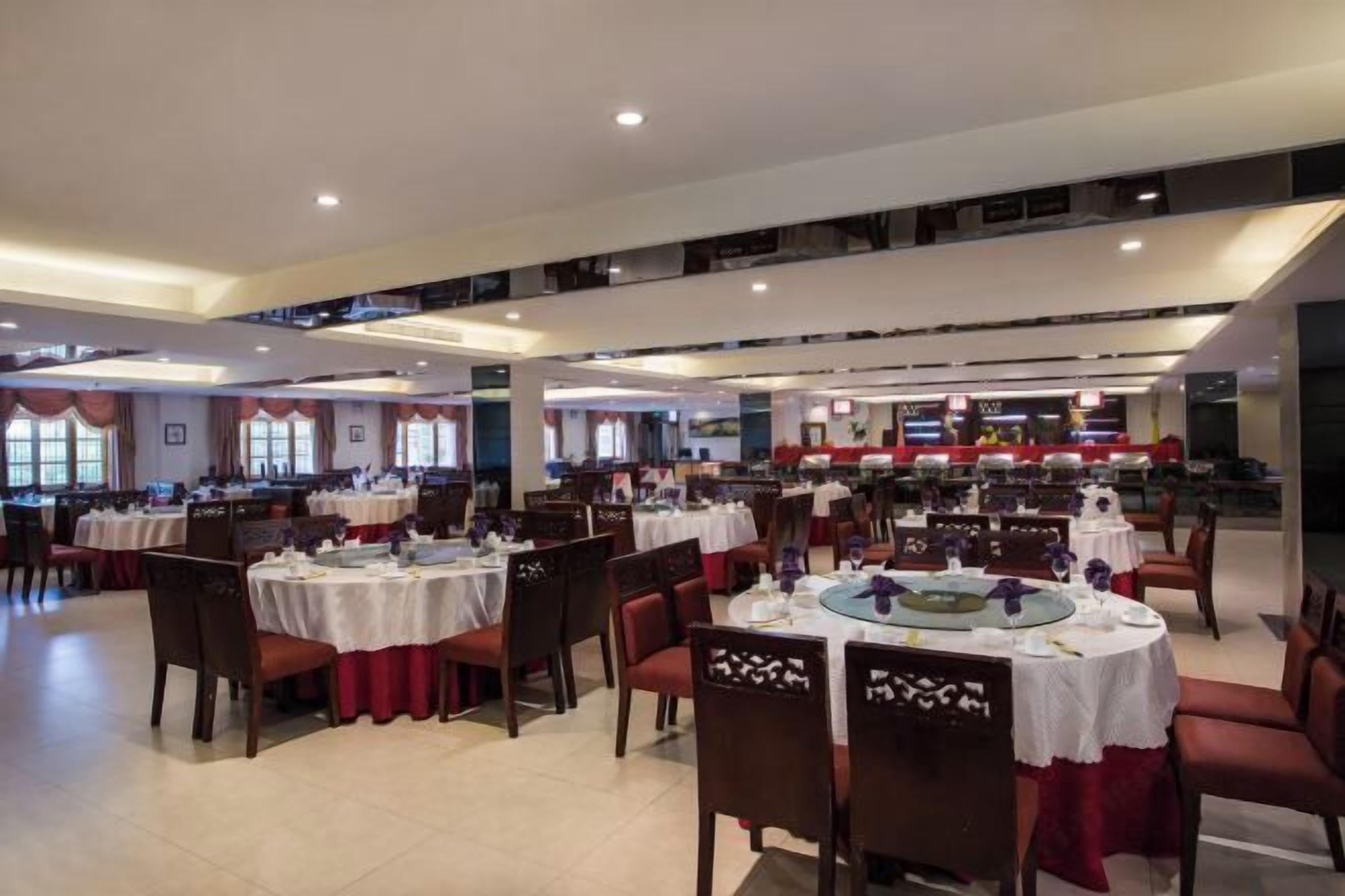 A spacious dining area with multiple round tables, each set with white tablecloths and red curtains.